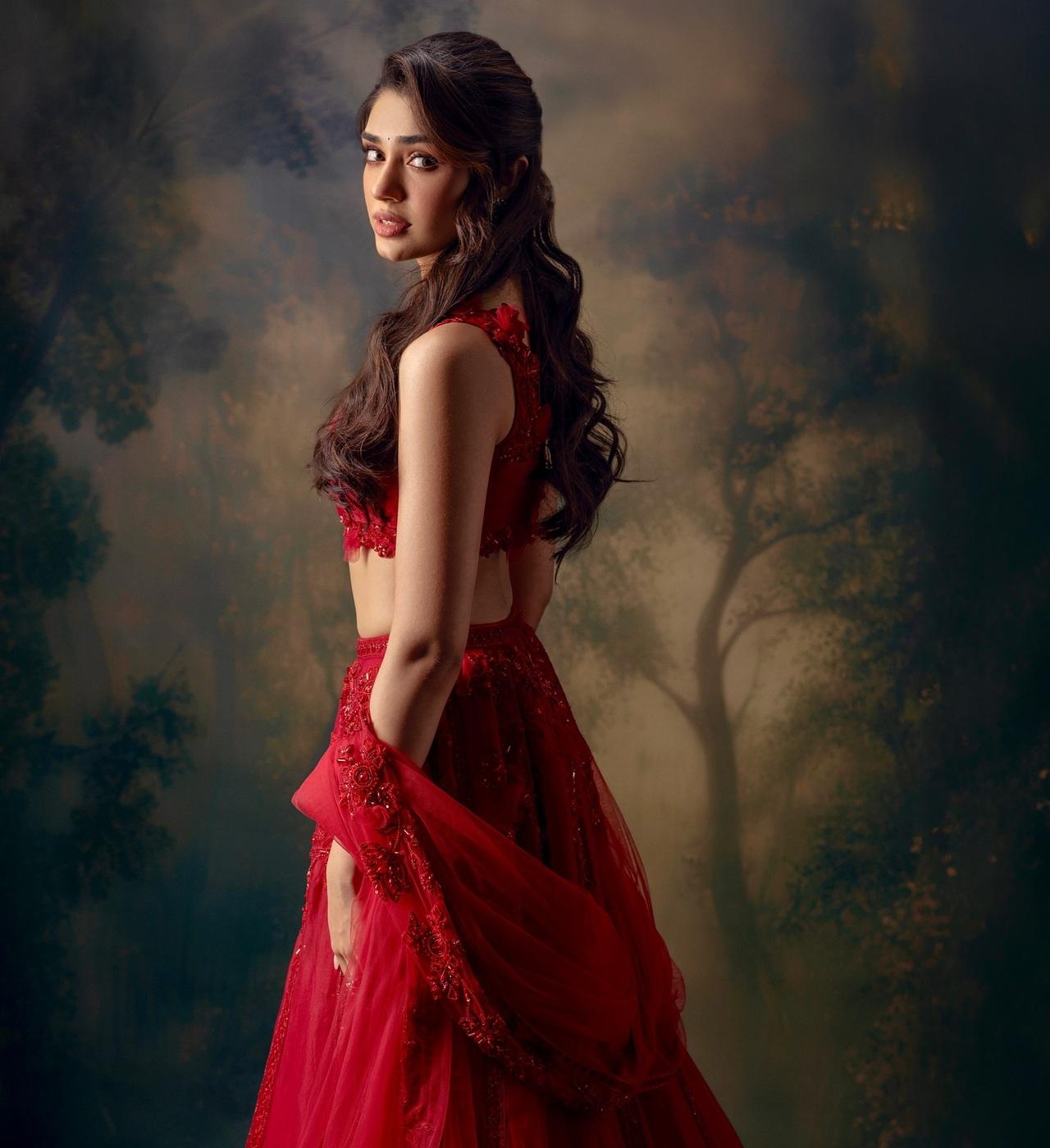 Krithi Shetty stuns in a regal red lehenga adorned with intricate embellishments that balance a modern yet traditional look. She opts for soft makeup as she amps up the glam quotient. 